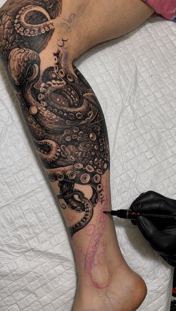 Artist drawing octopus tentacle outline with marker on client leg