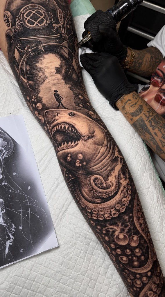 Artist working on diving helmet and shark tattoo during a session